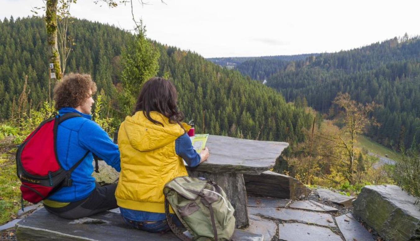 2 Menschen sitzen vor einer Aussicht am Berg